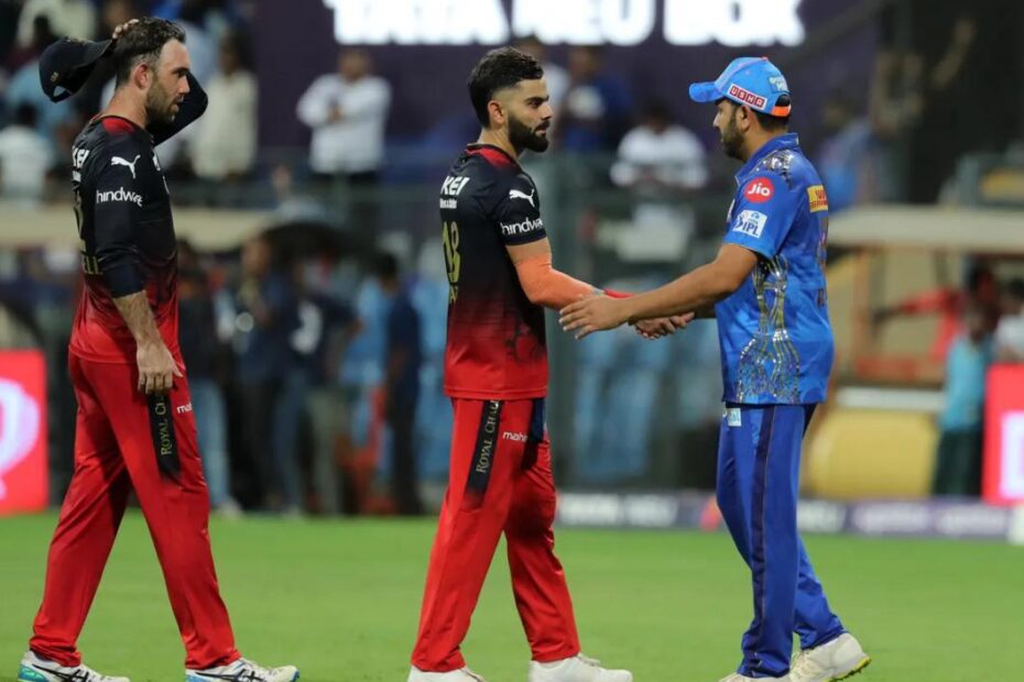 Two cricket players shake hands on the field before a match; a blue-jersey player greets a red-and-black team member while a third player walks by in the background.